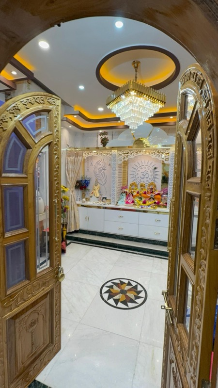 Mandir interior with carved wooden entry, chandelier and devotional wall panel